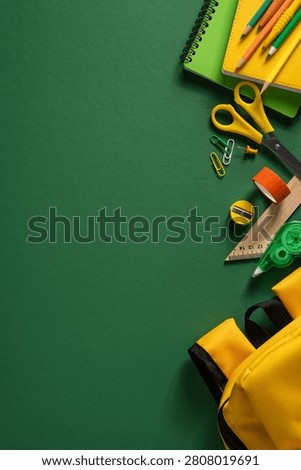 Back to school flatlay featuring a yellow backpack, green notebooks, pencils and assorted stationery arranged on a green background