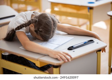 Back to school, the girl lies and rests on her school desk in the classroom after school. The schoolgirl is tired from classes and wants to sleep. Heavy workload at school.  - Powered by Shutterstock