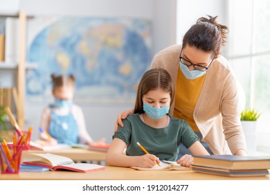 Back to school. Happy children are wearing facemasks sitting at desks. Girls with teacher in classroom. - Powered by Shutterstock