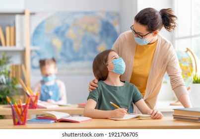 Back to school. Happy children are wearing facemasks sitting at desks. Girls with teacher in classroom. - Powered by Shutterstock