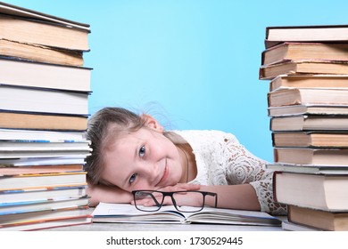 Back to school .Happy cute industrious child is sitting at a desk indoors. Kid is learning in class learning in home.Mountains of books on the sides.