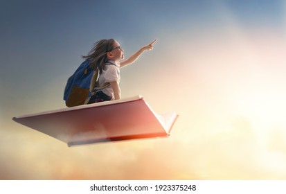 Back to school! Happy cute industrious child flying on the book on background of sunset sky. Concept of education and reading. The development of the imagination. - Shutterstock ID 1923375248