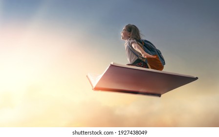 Back to school! Happy cute industrious child flying on the book on background of sunset sky. Concept of education and reading. The development of the imagination. - Shutterstock ID 1927438049