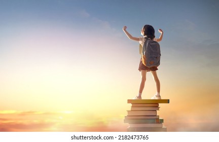 Back to school! Happy cute industrious child standing on the tower of books on background of sunset sky. Concept of education and reading. The development of the imagination. - Powered by Shutterstock