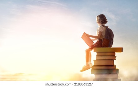 Back to school! Happy cute industrious child sitting on the tower of books on background of sunset sky. Concept of education and reading. The development of the imagination. - Shutterstock ID 2188563127