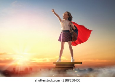 Back To School! Happy Cute Industrious Child Standing On The Tower Of Books On Background Of Sunset Sky. Girl Is Wearing Superhero Cape. Concept Of Success Education And Reading.