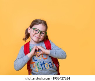 Back To School. Happy Kid Girl In Glasses With Backpack Showing Heart With Hands. Friendship Concept. Smiling Little Child Smiling In Love With Heart Symbol Romantic Concept