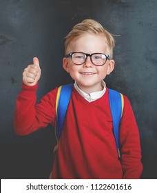 Back To School. Happy Little Boy In Glasses With Thumb Up And Backpack Against Blackboard. 