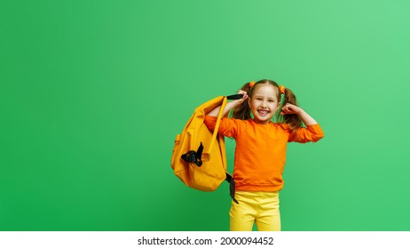 Back to school. happy little schoolgirl with two ponytails, in fashionable clothes and with backpack shows off her muscles. confident, strong and successful girl smiles and poses on green background. - Powered by Shutterstock