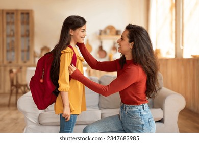 Back to School. Happy middle eastern mom preparing preteen schoolgirl daughter with backpack for first school day at home, looking at kid and encouraging her to enjoy classes in the morning
