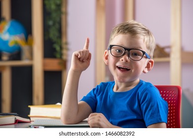Back to school. Happy pupil in glasses and uniform in class ready to answer on teachers question. Portrait of smiling boy face sitting on desk. Education, success, innovation, teaching concept. 