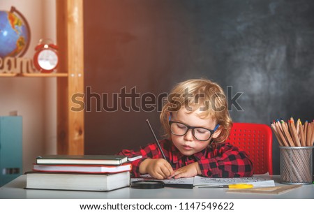 Back to school. Happy smiling pupil drawing at the desk. Child in the class room with blackboard on background. Alarm clock, pencils, books. Kid girl from primary school. first day of fall.