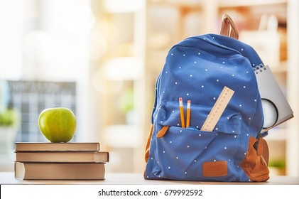 Back to school and happy time! Apple, pile of books and backpack on the desk at the elementary school.  - Shutterstock ID 679992592