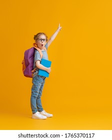 Back To School And Happy Time! Cute Industrious Child On Color Paper Wall Background. Kid With Backpack. Girl Ready To Study.