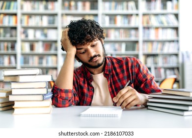 Back To School. Indian Or Arabian Bored Tired Male Student, Sitting At The Table With Books In The University Library, Takes Notes In A Notebook, Looking Sad And Exhausted From Studying, Needs A