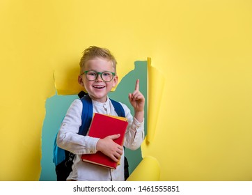 Back To School. Industrious Child Boy With Backpack And Books. Happy Kid Is Breaking Paper Wall. Funny Pupil In Glasses Pointing Up