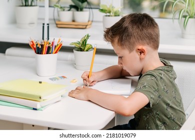 Back to school. Kid boy studying at home with book, writing in notepad and doing school homework. Thinking caucasian child siting at table with notebook. Distance learning online education.