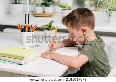 Back to school. Kid boy studying at home with book, writing in notepad and doing school homework. Thinking caucasian child siting at table with notebook. Distance learning online education.