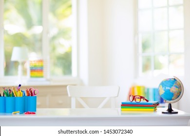 Back to school. Kids bedroom with wooden desk, books, globe, backpack, glasses and pencils. White room with big window for young child. Home interior for girl or boy. Table for homework and study.