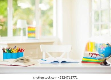 Back to school. Kids bedroom with wooden desk, books, globe, backpack, glasses and pencils. White room with big window for young child. Home interior for girl or boy. Table for homework and study. - Powered by Shutterstock