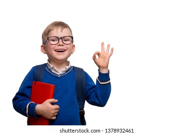 Back To School. Little Boy In Glasses With Bag And Book Shows OK Or Alright Sign. Success And Happy Kid Isolated On White. Child From Elementary School With Book. Education.