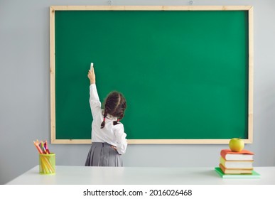 Back to school. Little schoolgirl writes on the school blackboard with chalk in the classroom. - Powered by Shutterstock