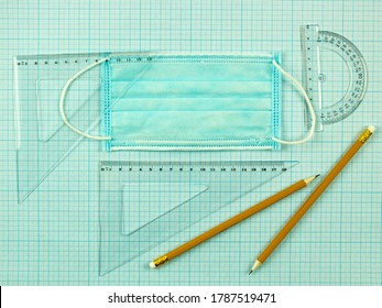 Back To School And A Medical Mask. Social Distance And Education. Scaled Coordinate Paper, Ruler, Protractor And Pencil