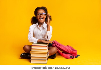 Back To School. Nerdy Schoolgirl Raising Hand During Class Sitting At Books Over Yellow Studio Background. Free Space