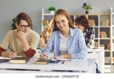 Back To School And Offline Education Concept. Pretty Happy Smiling Caucasian Teenage Female Student Writing In Notebook And Looking At Camera. Pupils Of Highschool Or College Studying In Classroom