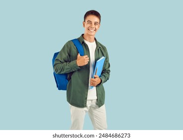 Back to school. Portrait of joyful smiling boy student with backpack and notebook on light blue background. Caucasian schoolboy teenager in casual clothes smiling broadly at the camera. Isolated. - Powered by Shutterstock