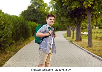 Back To School. Portrait Of Smiling Boy Who Goes To School In Park With His School Backpack On Warm Morning. Caucasian Schoolboy In Summer Casual Clothes Posing On Sidewalk In City Park.