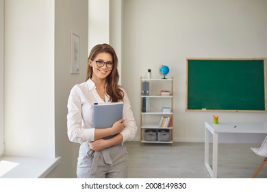 Back to school. Positive teacher woman with glasses standing with notebook in school class. Learning education care parenting. - Shutterstock ID 2008149830