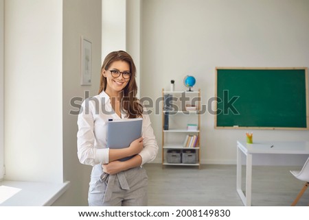 Back to school. Positive teacher woman with glasses standing with notebook in school class. Learning education care parenting.