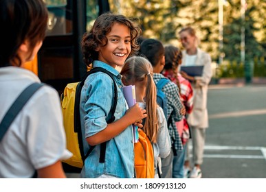 Back to school. Pupils of primary school with teacher near school bus. Happy children ready to study. - Shutterstock ID 1809913120