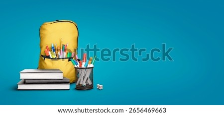 A back to school scene of a pile of three study books to learn from, yellow school bag and pens and pencils against a blue background with copy space.