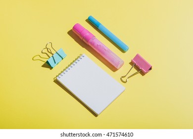 back to school set: two markers, two paper clips and notepad on yellow background