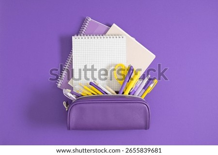 Back to school. A stack of notepads and notebooks and a purple pencil case filled with pens and pencils. School educational theme.