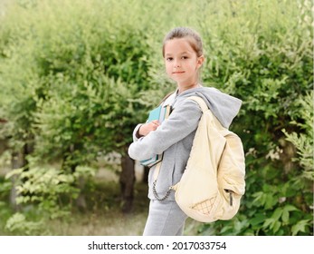 Back to school. A student outside with a backpack smiling, holding a book.