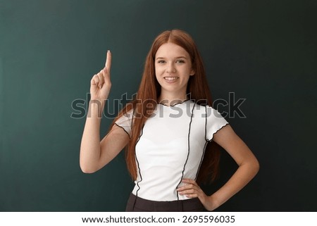 Back to school. Student pointing at something near green chalkboard indoors