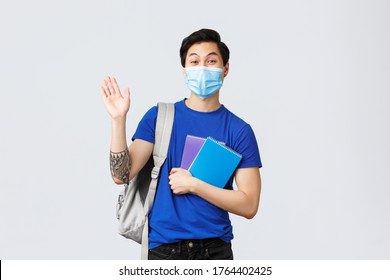 Back To School, Studying During Covid-19, Education And University Life Concept. Young Handsome Asian Male Student, Freshman In College Waving Hand In Hello Or Greeting, Holding Notebooks