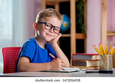 Back To School. Thinking Child Boy Writing, Drawing In Notebook Sitting At Desk And Doing Homework. Pupil Of Primary School In Class Writing And Reading. Home Schooling And Education At Home