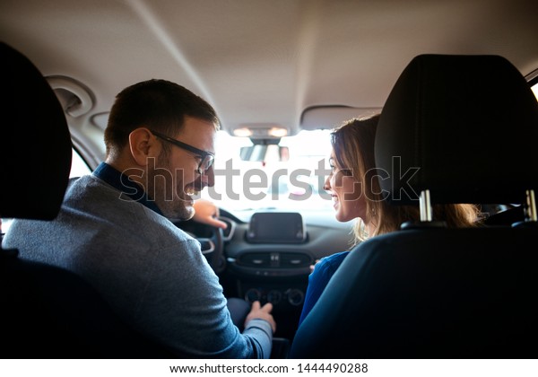 Back seat view of car interior and lovely couple\
sitting in front of the car looking at each other and smiling.\
Family buying perfect car.