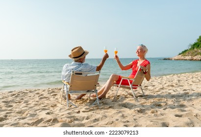 Back of senior man hold glass of orange juice and cheers to his wife during sit on beach chair and relax on holiday or vacation time. - Powered by Shutterstock