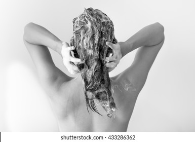 The Back Of A Sexy Fit Woman Washing Her Hair Full Of Suds In Front Of A White Background