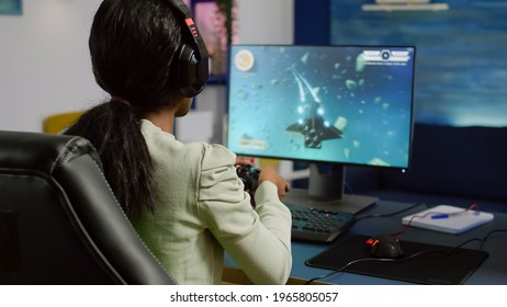 Back Shot Of Pro Black Woman Streamer Winning Graphics Cyber Space Shooter Video Games Using Wireless Joystick. Gamer Performing On Powerful Pc Talking With Players On Chat Open During Competition