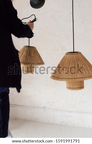 Back shot of white man installing straw lamps at home. Interiors design concept with negative space. Tendencies and interiorism stills.