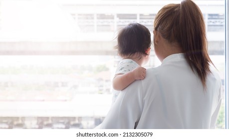 Back Side, Asian Mother Holding Baby To Look Outside The Window On Sunny Day.