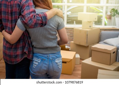 Back Side Of Asian Young Couple Hugging Together Over The Big Cardboard Box And Sofa When Moving In New House, Moving And House Hunting Concept