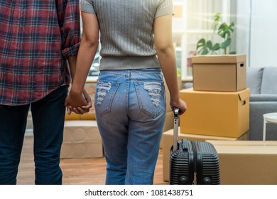 Back Side Of Asian Young Couple Holding One's Hands And Luggage Over The Big Cardboard Box And Sofa When Moving In New Home, Moving And House Hunting Concept