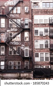 Back side of a brick apartment building in Manhattan, showing the fire escape and graffiti on its facade. 